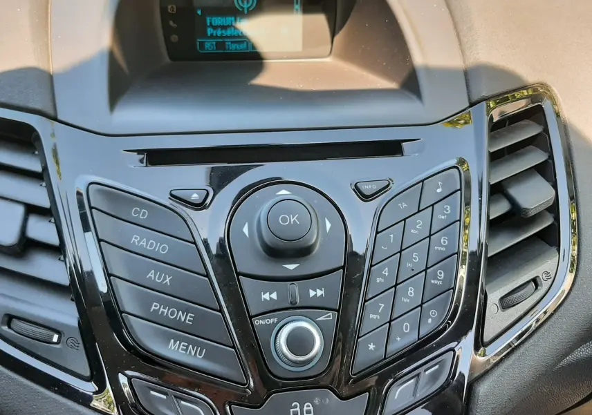 Vue rapprochée de la console centrale noire brillante de la Ford Fiesta marron métal, avec commandes audio et écran digital.