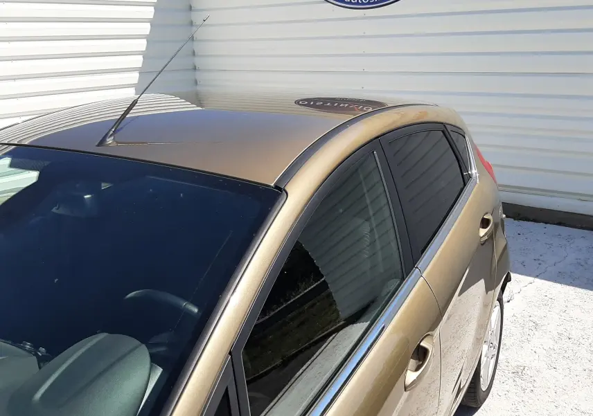Vue 3/4 avant droit d'une Ford Fiesta marron métal 5 portes avec vitres teintées, garée devant un mur blanc.
