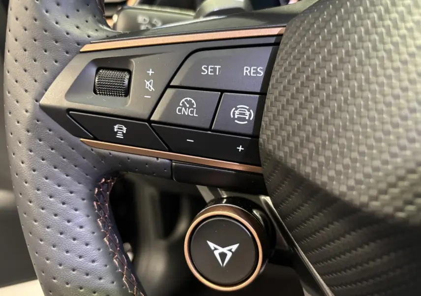 Gros plan sur le volant perforé noir avec surpiqûres cuivrées et commandes multifonctions du CUPRA Leon gris Magnetic.