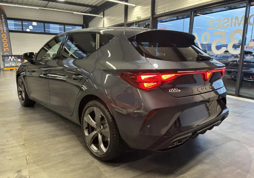 Vue 3/4 arrière droite d'une CUPRA Leon gris magnetic avec feux arrière Tri-LED et jantes anthracite 18 pouces.