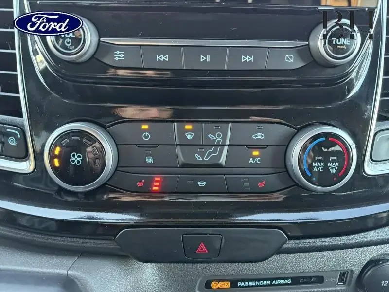 Vue rapprochée de la console centrale noire du Ford Transit Custom 2023, avec commandes climatisation et boutons éclairés.