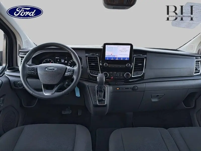 Vue intérieure avant du Ford Transit Custom 2023, tableau de bord noir avec écran tactile central et volant cuir.
