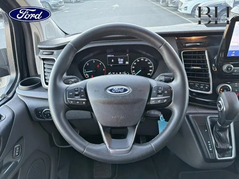 Vue intérieure centrée sur le volant cuir noir du Ford Transit Custom 2023 avec tableau de bord et levier de boîte auto.