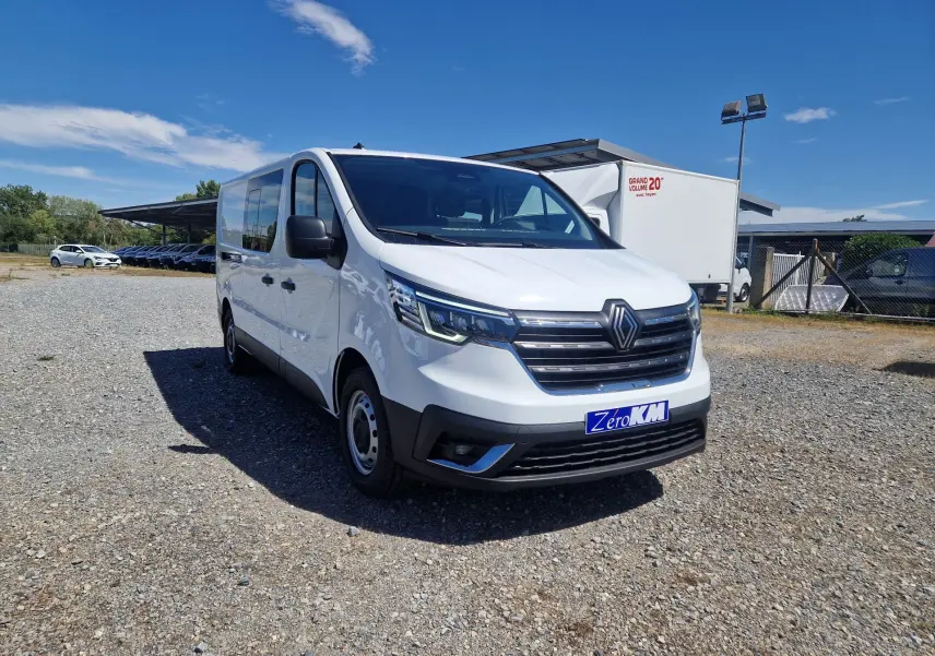 Renault Trafic cabine approfondie blanc en 3/4 avant droit sur parking extérieur sous ciel bleu.