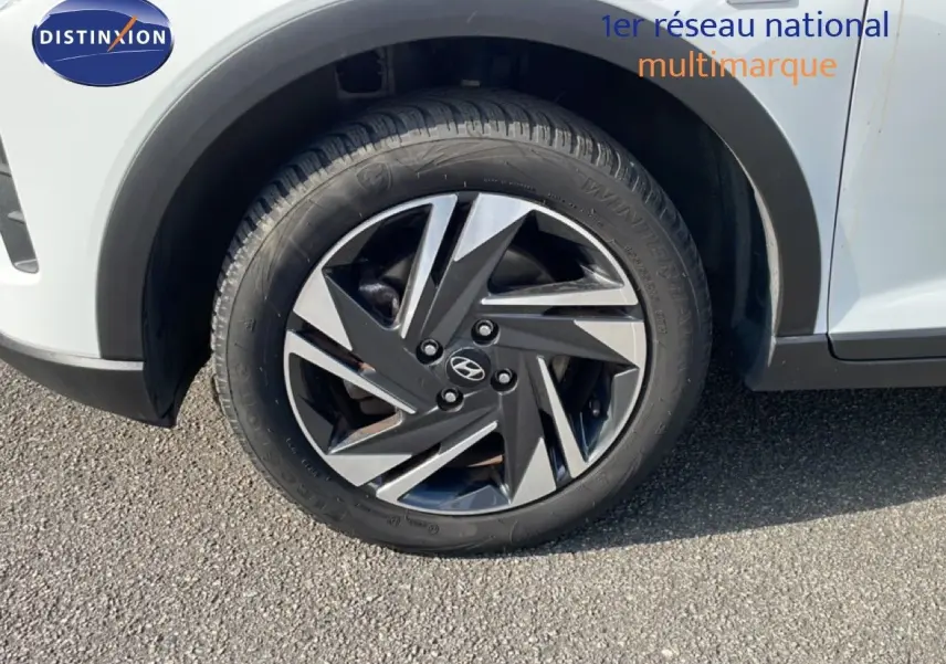 Gros plan sur la roue avant droite d’une Hyundai Bayon blanche polaire avec jante alliage bicolore et badge Hyundai.
