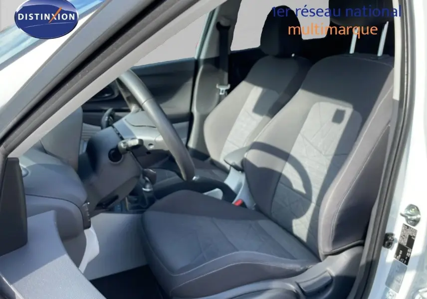 Vue intérieure côté conducteur du Hyundai Bayon blanc polaire, mettant en valeur les sièges tissu gris et le volant multifonction.