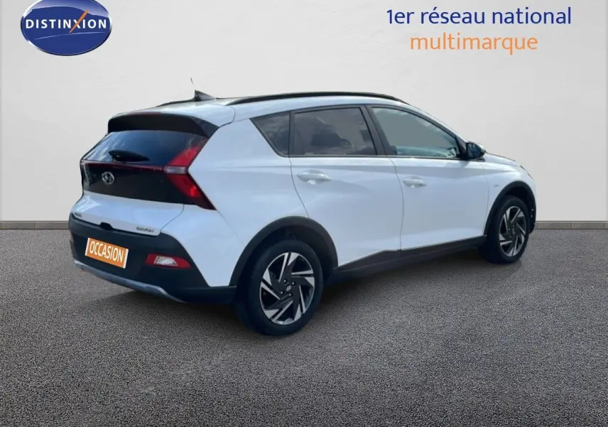 Vue 3/4 arrière droite d'une Hyundai Bayon blanche polaire avec jantes noires et détails noirs contrastants.