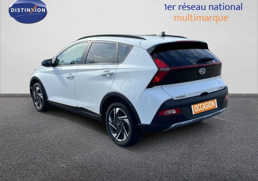 Vue 3/4 arrière droite du Hyundai Bayon blanc polaire avec toit noir et feux arrière en bandeau lumineux.