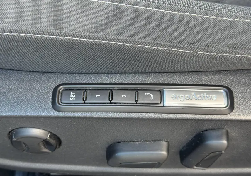 Gros plan sur les commandes de réglage mémoire ergoActive du siège avant côté conducteur, tissu gris.