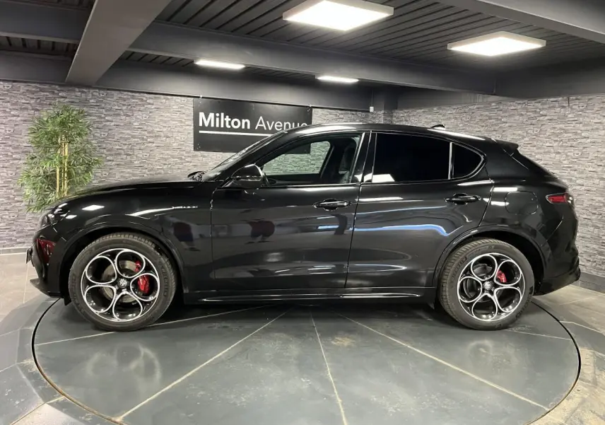Profil côté gauche d'un Alfa Romeo Stelvio Veloce 2024 noir métallisé avec jantes 20 pouces et étriers rouges Brembo.