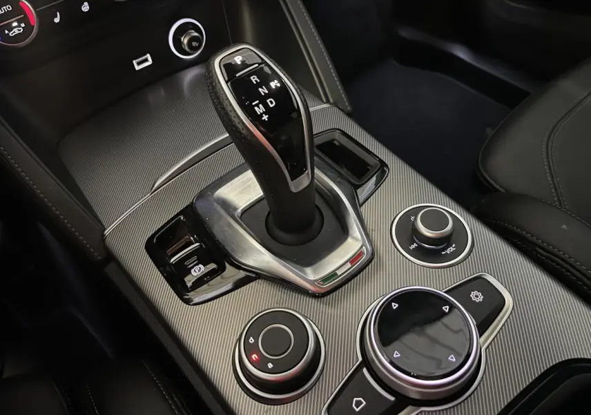 Gros plan sur la console centrale de l'Alfa Romeo Stelvio Veloce 2024 avec levier de vitesse automatique et commandes en finition carbone.