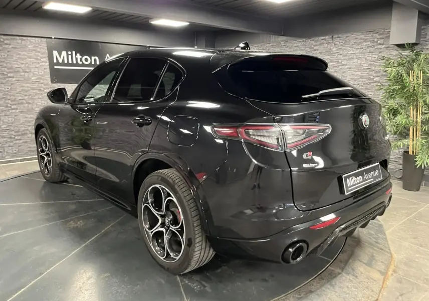 Vue 3/4 arrière côté gauche d'un Alfa Romeo Stelvio Veloce noir métallisé avec jantes 20 pouces et double sortie d'échappement noire.