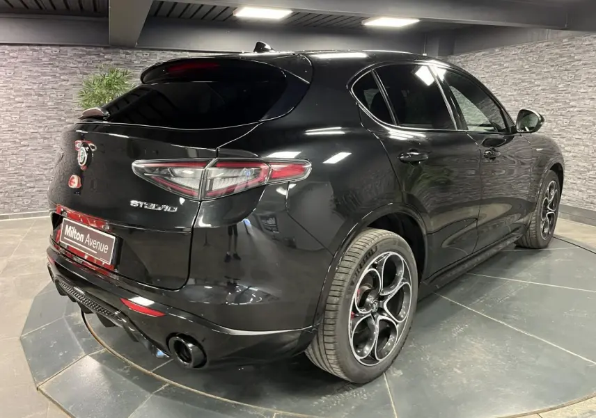 Vue 3/4 arrière droite de l'Alfa Romeo Stelvio noir Vulcano avec jantes 20 pouces et double sortie d'échappement noire.