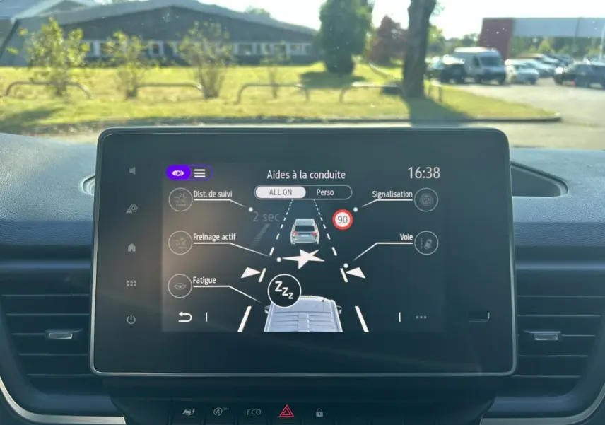 Vue intérieure côté conducteur du Renault Trafic Fourgon gris urbain, montrant les sièges avant et le tableau de bord moderne.