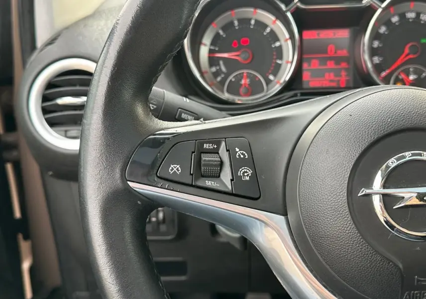 Gros plan sur le volant cuir de l'Opel Adam marron, mettant en valeur les commandes du régulateur de vitesse.