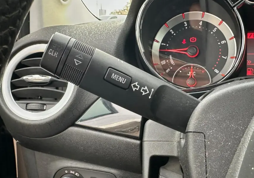 Détail du commodo de clignotant et du tableau de bord avec compte-tours rouge sur Opel Adam marron, vue intérieure côté gauche.