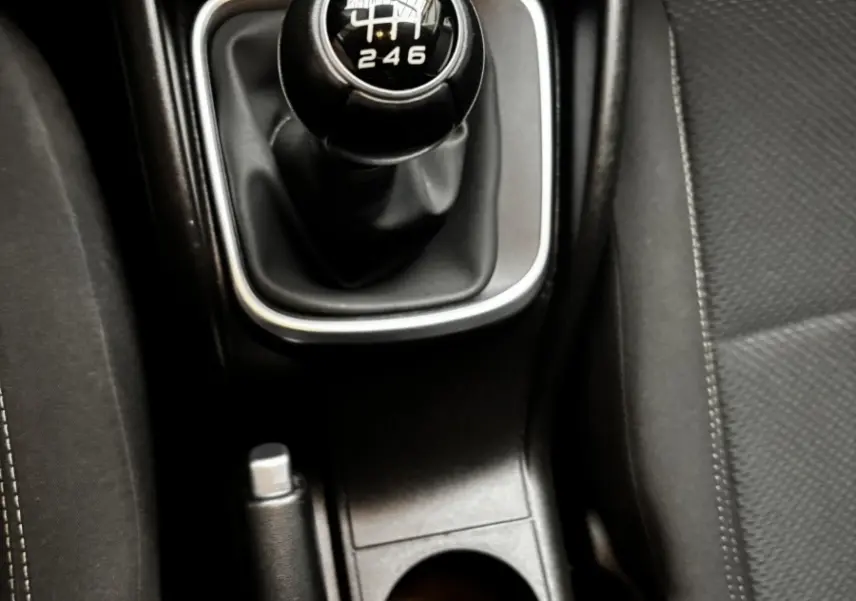 Gros plan sur le levier de vitesses manuel noir et la console centrale entre les sièges avant gris foncé du Fiat Tipo blanc.