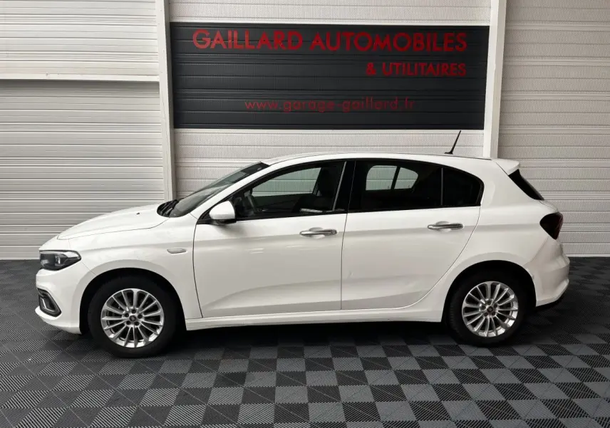Profil côté gauche d'une Fiat Tipo blanche 2021 garée en intérieur, soulignant ses jantes alliage et lignes épurées.