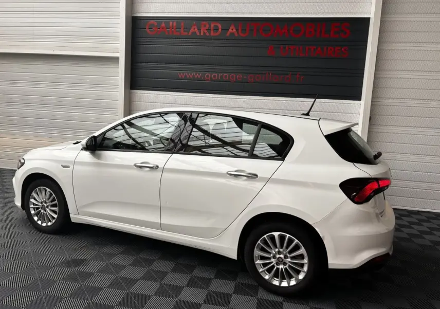 Profil côté gauche d'une Fiat Tipo blanche 2021, compacte, avec jantes alliage et feux arrière LED dans un garage.