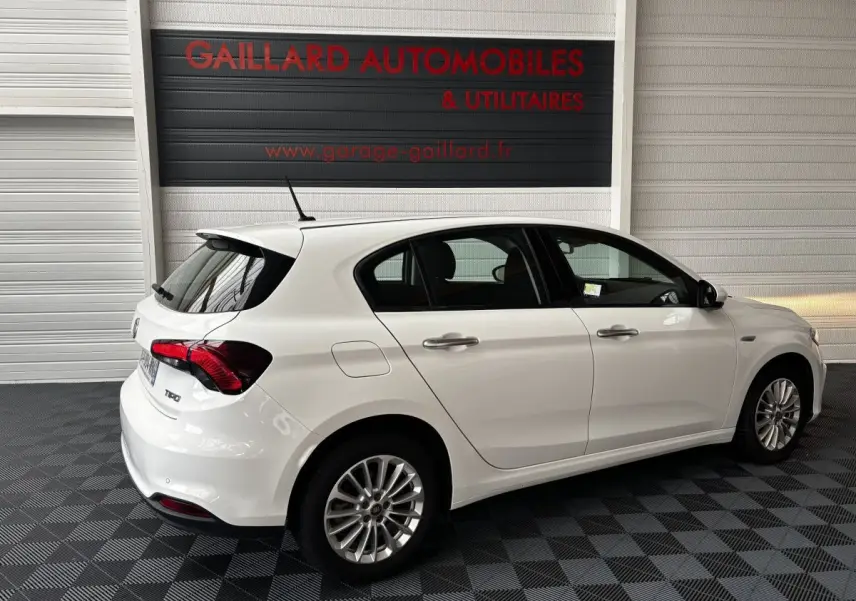Vue 3/4 arrière droite d'une Fiat Tipo blanche 5 portes garée en intérieur avec jantes alliage et feux arrière rouges.