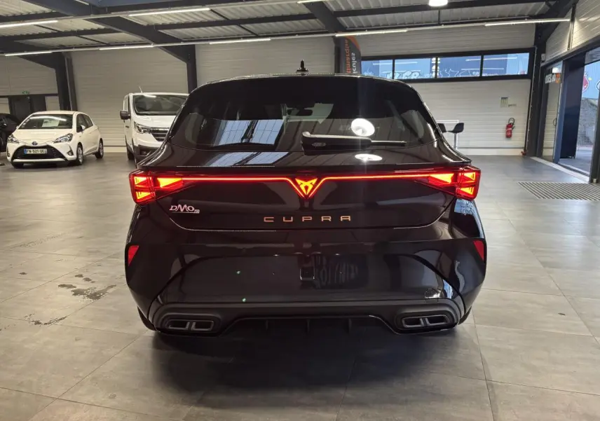 Vue arrière d'une CUPRA Leon noir midnight avec feux arrière Tri-LED allumés et double sortie d'échappement stylisée.