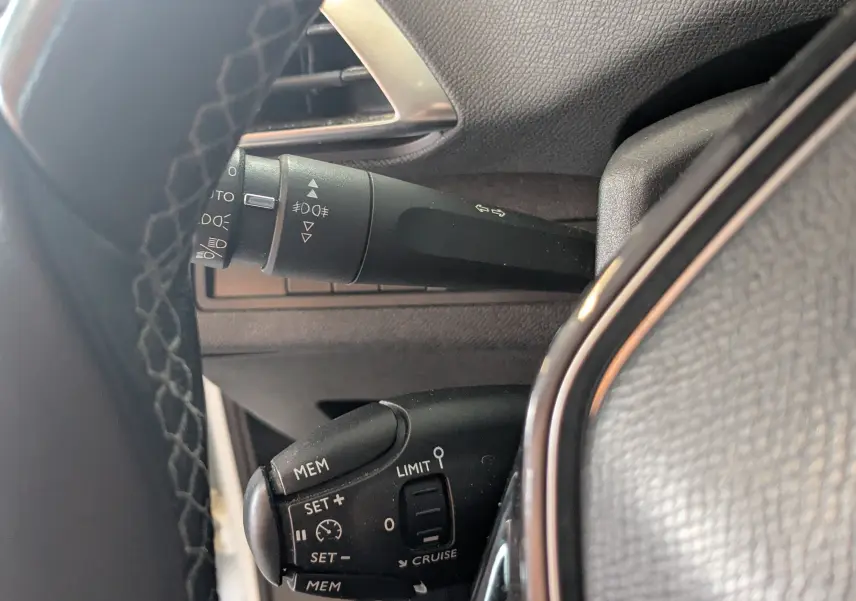 Gros plan sur les commandes au volant du Peugeot 3008 blanc toit noir, mettant en valeur les boutons de régulateur et clignotants.