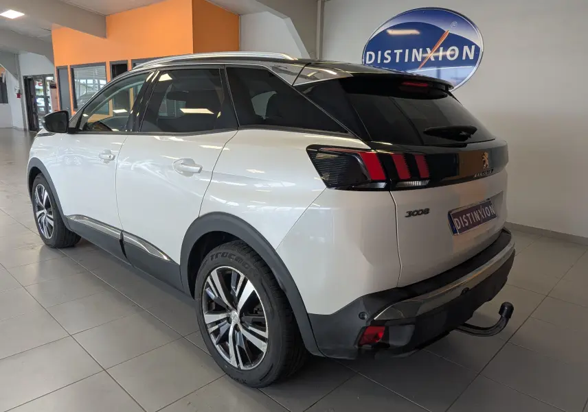 Vue 3/4 arrière droite du Peugeot 3008 blanc à toit noir avec attelage visible en intérieur showroom.