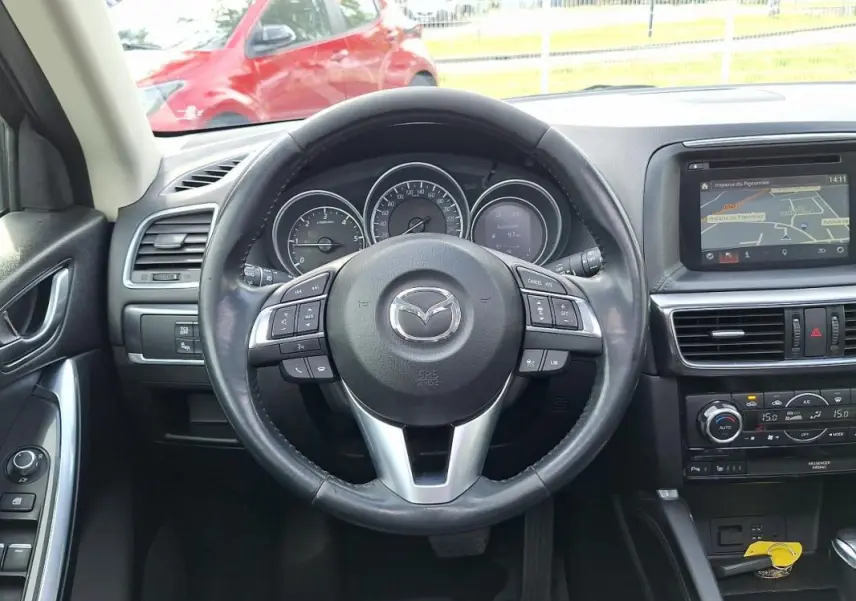 Vue intérieure centrée sur le volant cuir multifonctions et tableau de bord avec écran tactile GPS du Mazda CX-5 gris 2015.