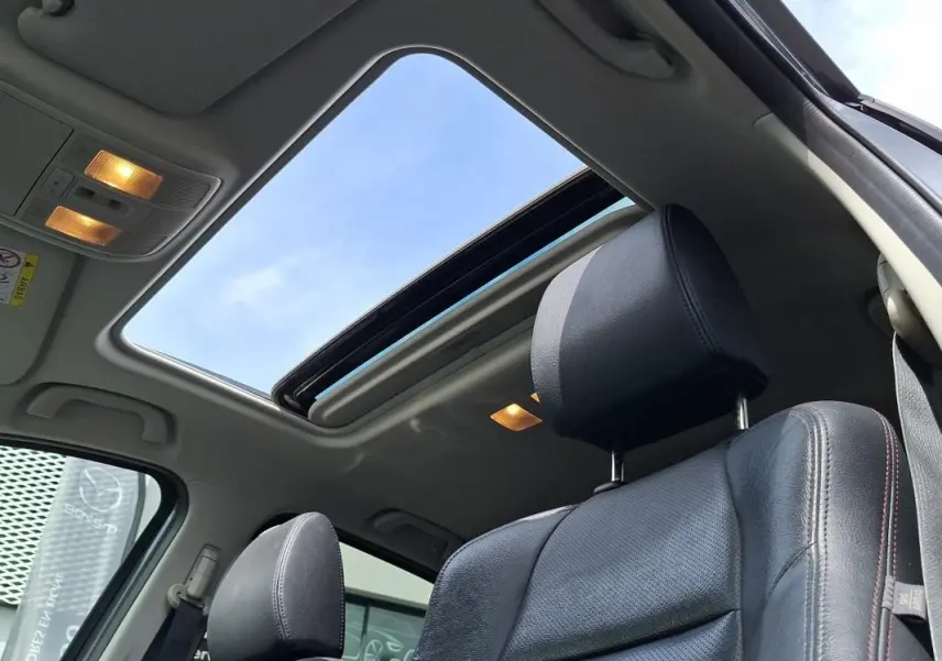 Vue intérieure du toit ouvrant électrique et siège avant cuir noir du Mazda CX-5 gris 2015 avec ciel bleu visible.