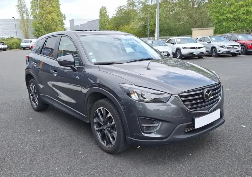 Vue 3/4 avant droit d'un Mazda CX-5 gris métallisé avec jantes alliage et vitres surteintées sur parking extérieur.