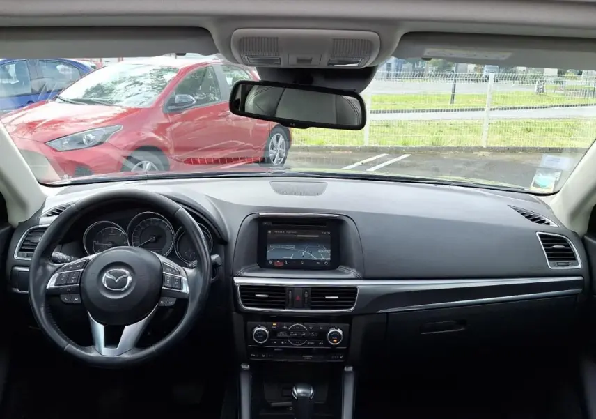 Vue intérieure avant du tableau de bord et volant cuir multifonctions de la Mazda CX-5 gris 2015 avec écran tactile GPS intégré.