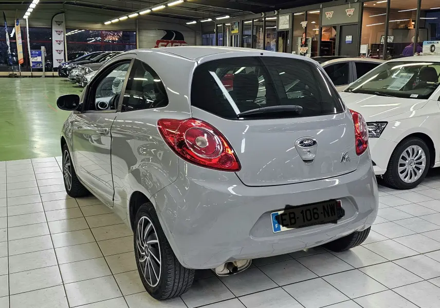 Vue 3/4 arrière droite d'une Ford KA+ grise 2016 avec feux arrière ronds et jantes alliage en intérieur showroom.