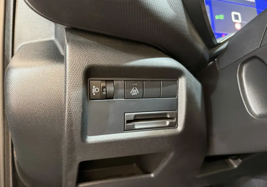 Gros plan sur les commandes de réglage des phares et d’aide à la conduite à gauche du volant dans un Citroën C5 Aircross gris clair 2023.