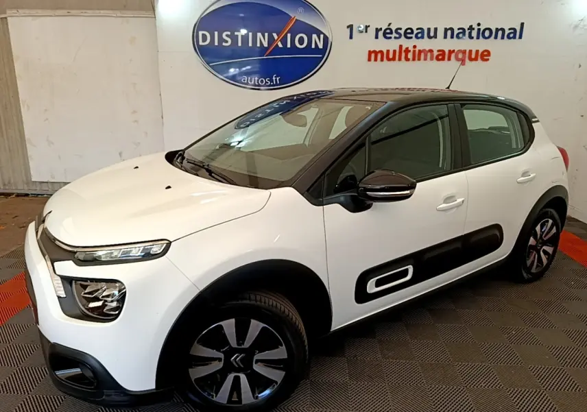 Vue 3/4 avant droite d'une Citroën C3 blanche avec protections latérales noires et jantes bicolores.