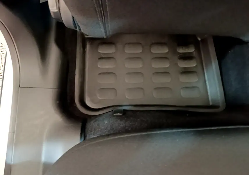 Vue rapprochée du tapis de sol arrière noir dans une Citroën C3 blanche, côté gauche, sous le siège passager.