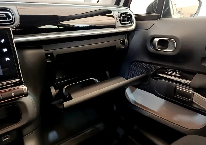 Intérieur de la Citroën C3 blanc, vue côté passager avec boîte à gants ouverte et tableau de bord noir brillant.
