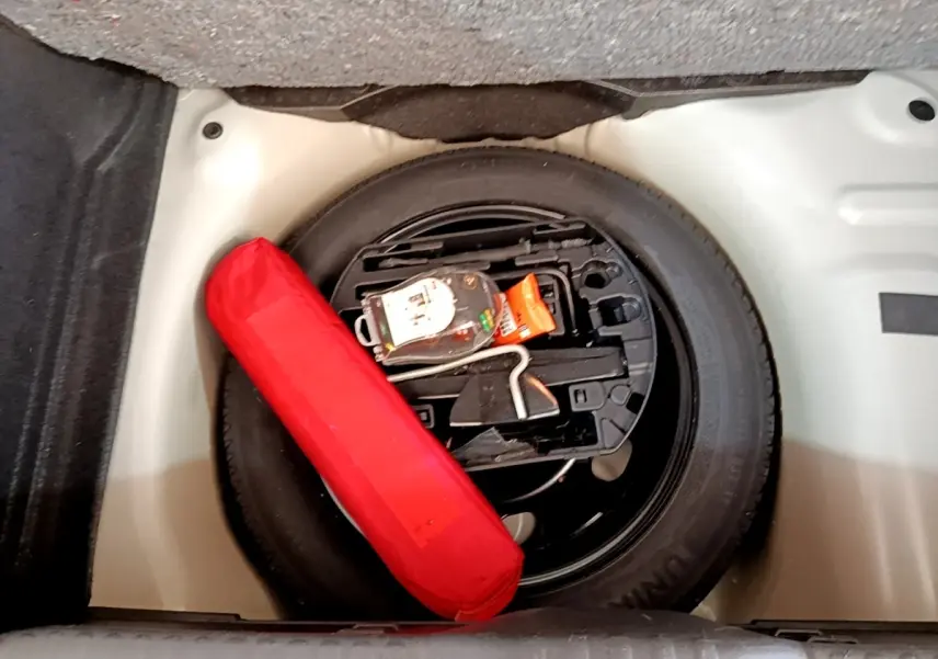 Vue plongeante sur la roue de secours noire et un triangle de signalisation rouge dans le coffre d'une Citroën C3 blanche.