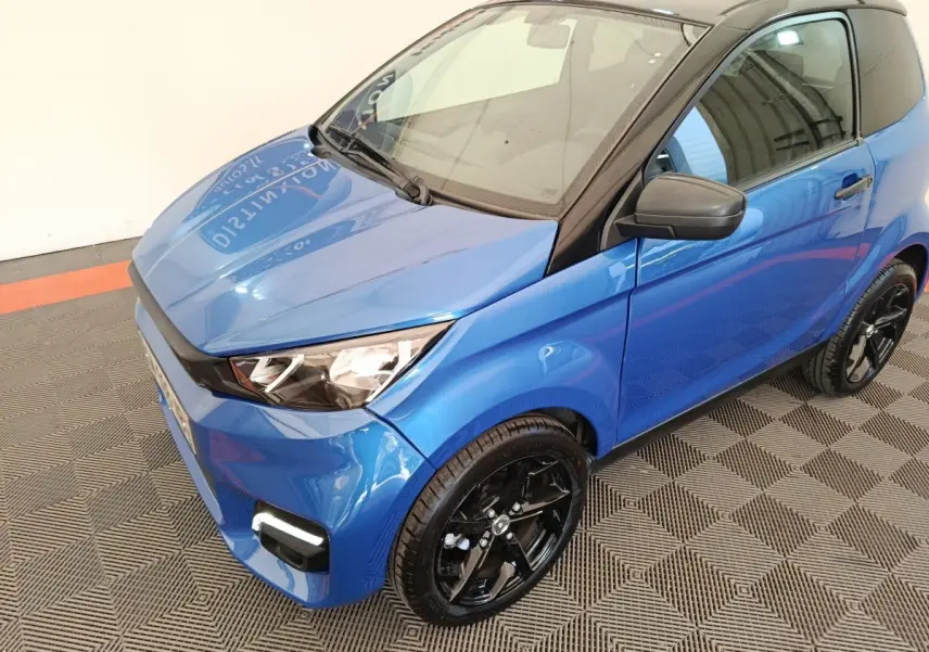 Vue 3/4 avant droit d'une Aixam Ambition 0.5 City Sport 2024 bleu avec rétroviseur côté conducteur noir et jantes noires.