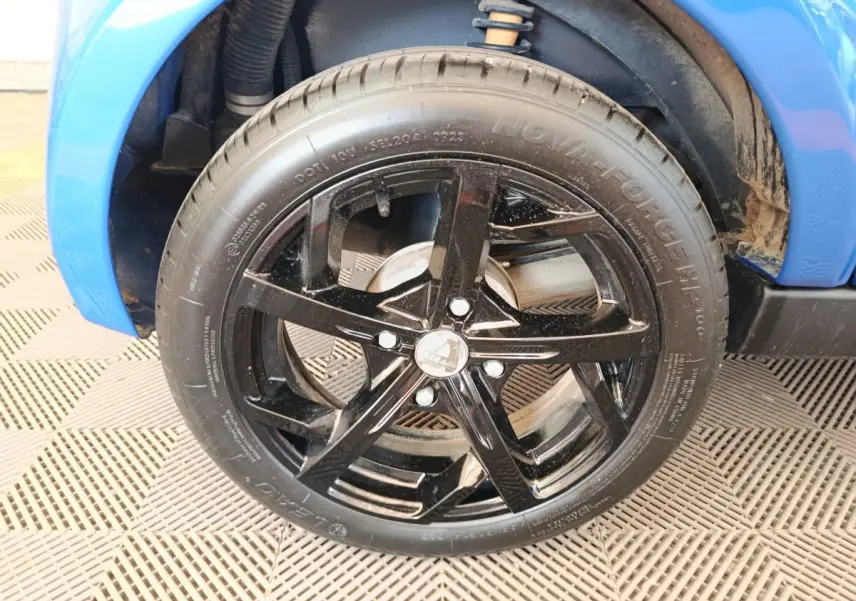 Gros plan sur la roue avant droite noire avec jante étoile du véhicule bleu Aixam Ambition 0.5 City Sport 2024.