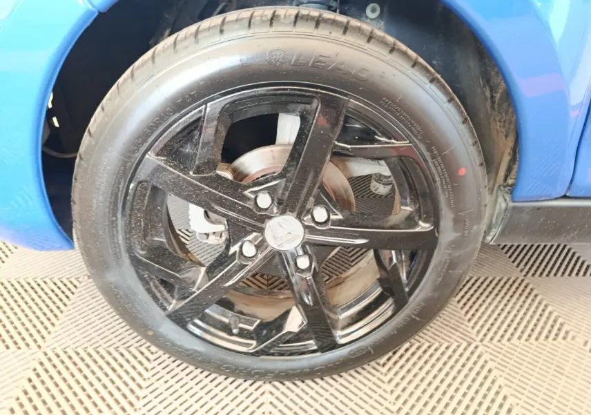 Gros plan sur la roue avant droite noire d'une Aixam Ambition 0.5 City Sport bleu 2024, avec jante à cinq branches.