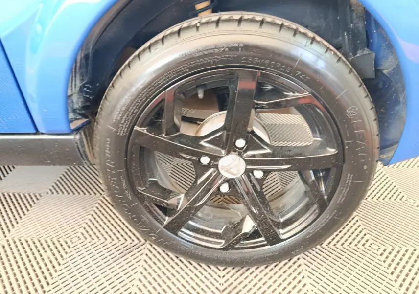 Gros plan sur la roue avant droite noire d'une Aixam Ambition 0.5 City Sport bleu 2024, avec partie de la carrosserie visible.