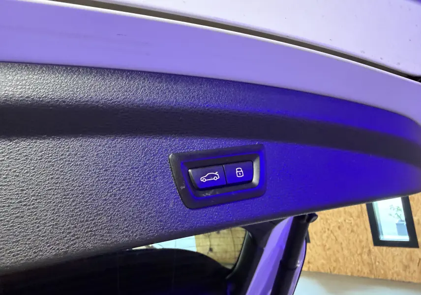 Gros plan sur les boutons de commande électrique du hayon du BMW X2 blanc, intérieur du coffre visible.