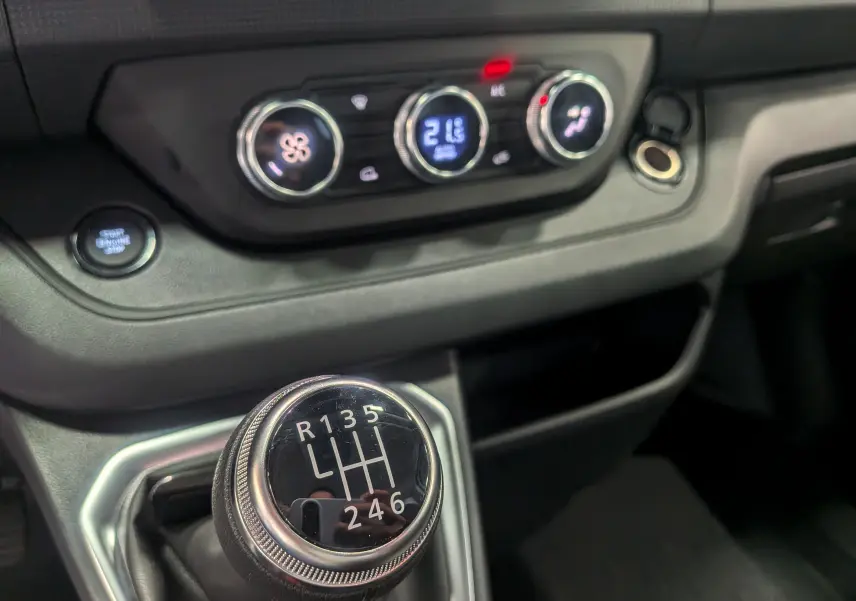 Gros plan sur la console centrale du Renault Trafic Fourgon L1H1 2025, avec levier de vitesse manuel et commandes de climatisation.