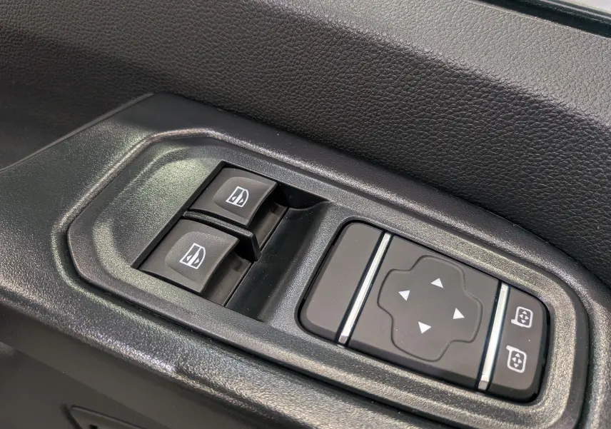 Gros plan sur les commandes électriques des vitres et rétroviseurs côté conducteur du Renault Trafic Fourgon blanc glacier 2025.