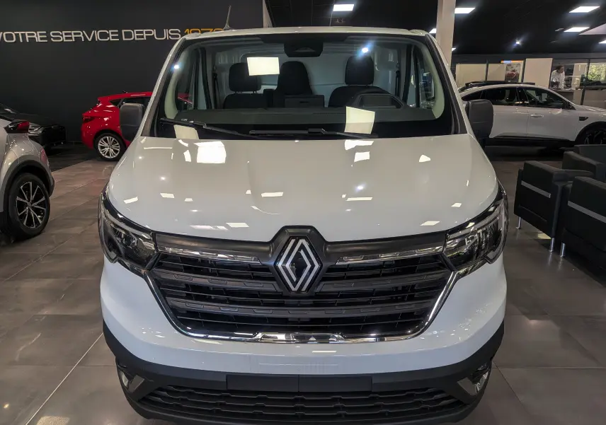 Vue frontale d'un Renault Trafic Fourgon blanc glacier 2025 avec calandre noire et logo Renault central visible.