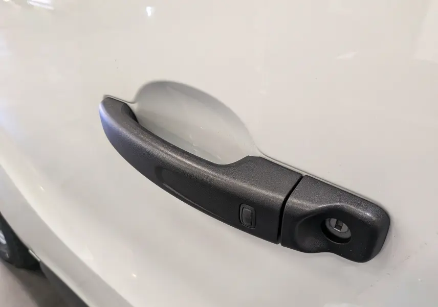 Poignée de porte noire en gros plan sur la portière blanche glacée d'un Renault Trafic Fourgon L1H1 2025.