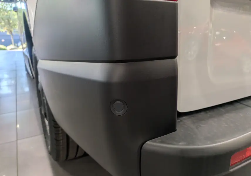 Gros plan sur le pare-chocs arrière droit noir du Renault Trafic Fourgon blanc glacier, avec capteur de recul visible.