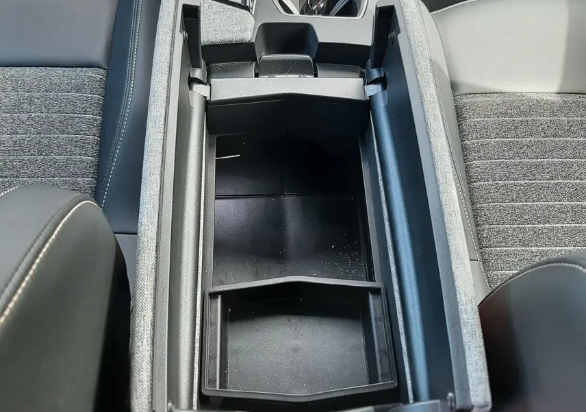 Vue plongeante sur le rangement central ouvert du Peugeot 5008 Hybrid gris titane, avec sièges tissu et cuir gris noir visibles.