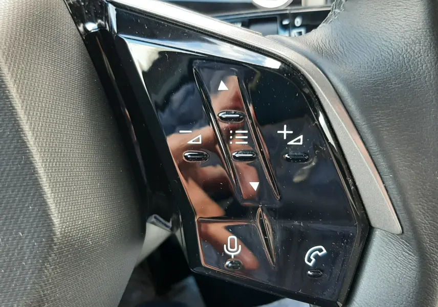 Gros plan sur les commandes noires au volant côté gauche du Peugeot 5008 Hybrid 145ch gris titane 2025.