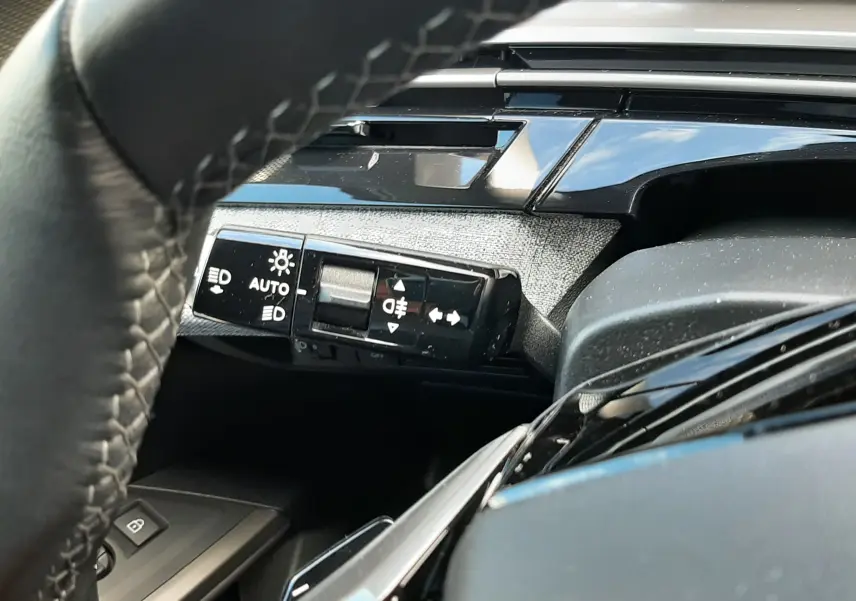 Gros plan sur la commande des feux et clignotants à gauche du volant dans l’habitacle gris noir du Peugeot 5008 Hybrid 2025.